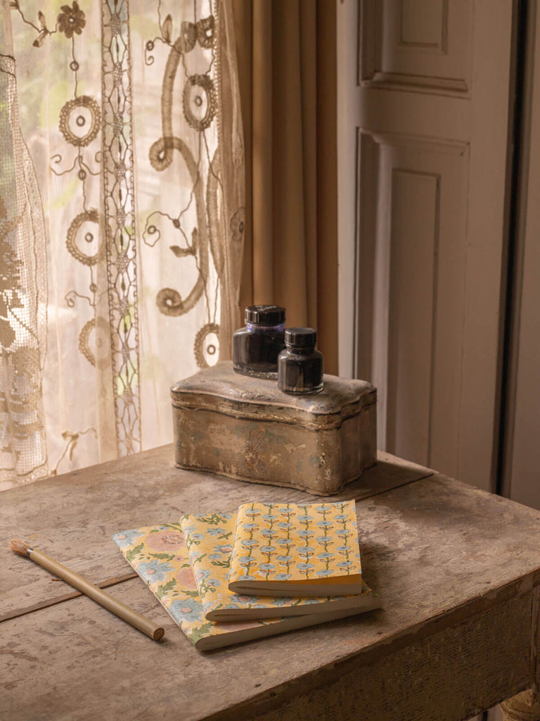 Group of buttermilk yellow and blue cotton paper notebooks with floral block print covers on an antique desk
