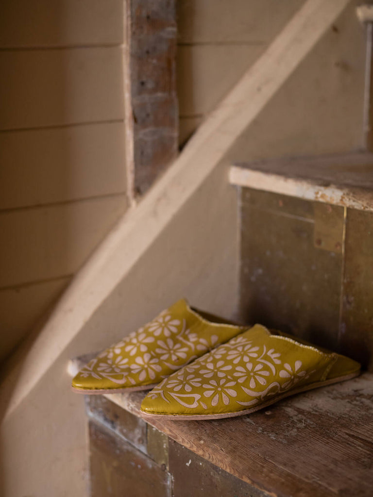 A pair of mustard decorative babouche slippers with daisy pattern on a rustic staircase