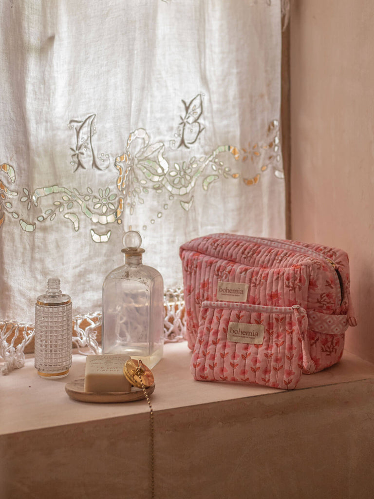 Vintage pink washbags of different sizes in a bathroom shelf next to handmade soap and antique bottles