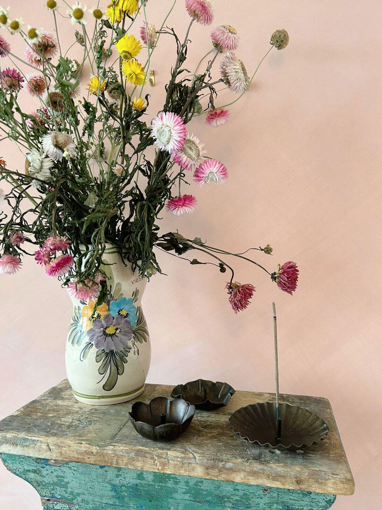 Three antiqued incense holders on a table with vase of dried flowers