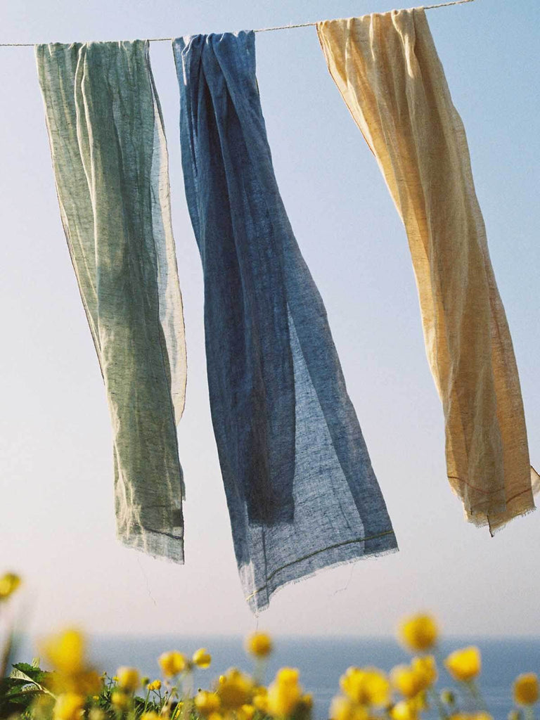 Three Bohemia linen scarves hanging on a washing line above yellow flowers