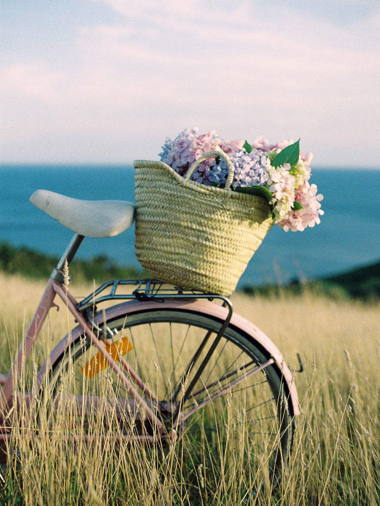 Natural woven market basket filled with flowers on the back of pink bicycle