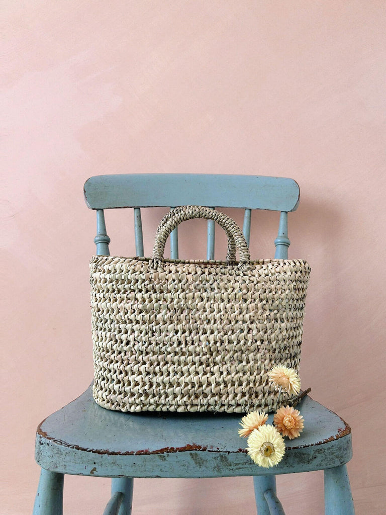 Small oval shaped natural woven nesting basket on a blue chair