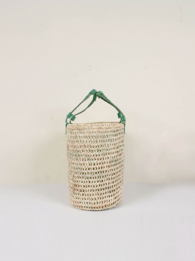 Side view to show the oval shape of the natural woven basket with sage green leather handles