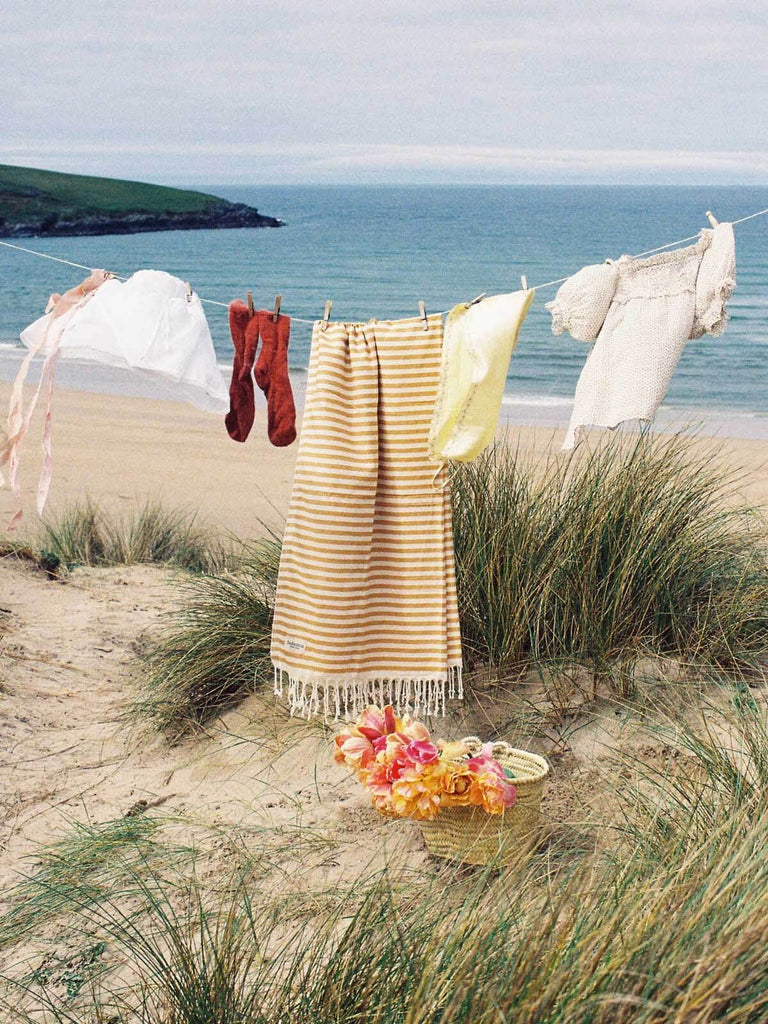 Classic stripe Sorrento Hammam Towel in Mustard hanging on a line by the sea