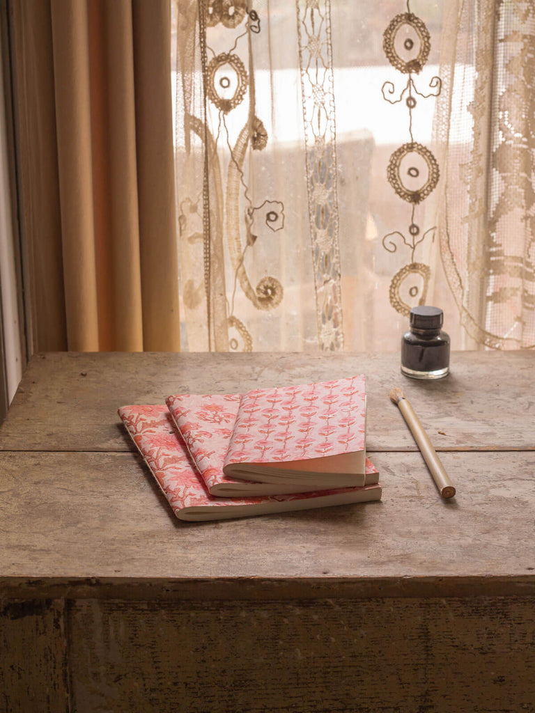 Group of vintage pink cotton paper notebooks with floral block print covers on an antique desk