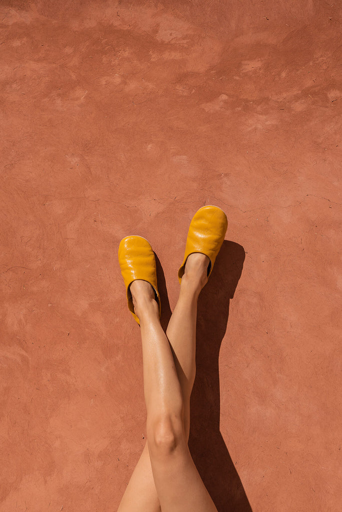 Bohemia-design-Moroccan-babouche-slippers-leather-mustard-model-against-terracotta-wall