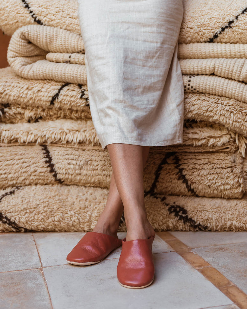 Women wearing Terracotta Moroccan babouche leather slippers by Bohemia Design against a stack cream berber rugs