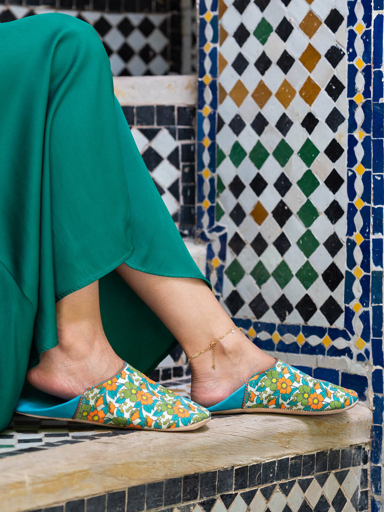 Woman wearing A pair of Moroccan babouche slippers in an aqua and orange floral pattern by Bohemia Design