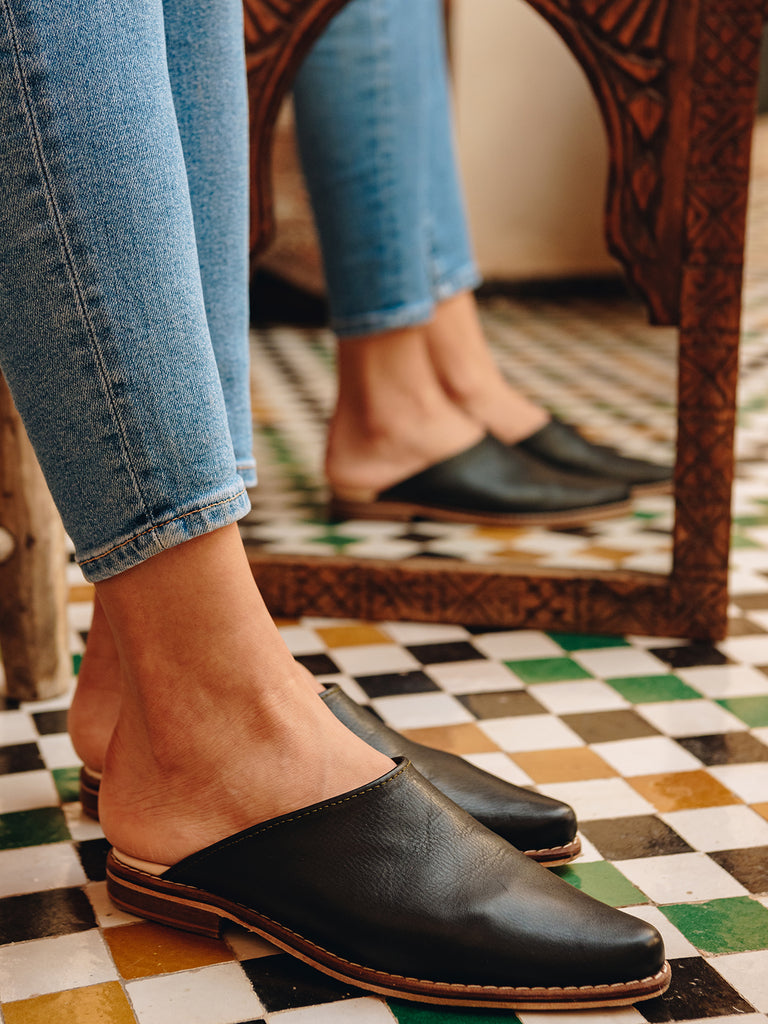 Woman wearing jeans and Leather mules in black leather by Bohemia Design on a Moroccan tiled floor