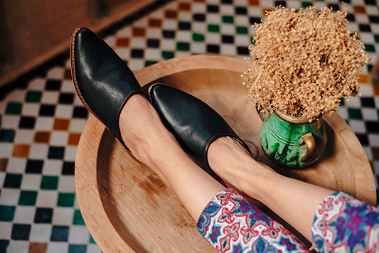 Woman wearing Leather mules in black leather by Bohemia Design with her feet up on a wooden coffee table