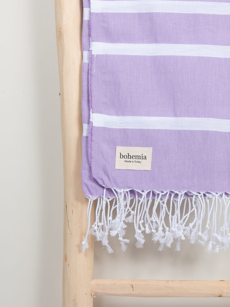 Ibiza Summer Hammam Towel in lilac stripe pattern by Bohemia Design hanging from a wooden ladder