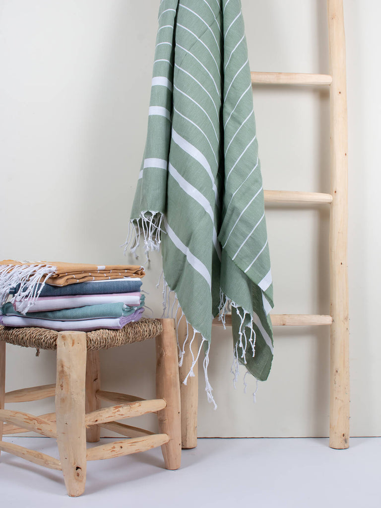 Ibiza Summer Hammam Towel in olive stripe pattern by Bohemia Design hanging on a wooden ladder