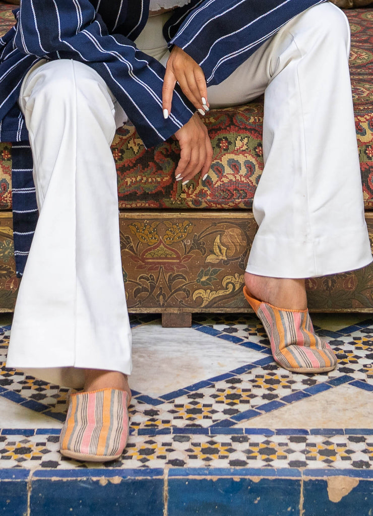 Woman wearing Moroccan babouche slippers in a tangerine stripe pattern by Bohemia Design on a Moroccan tiled floor