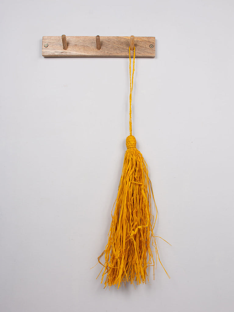 Yellow raffia tassel hanging on a wooden hook