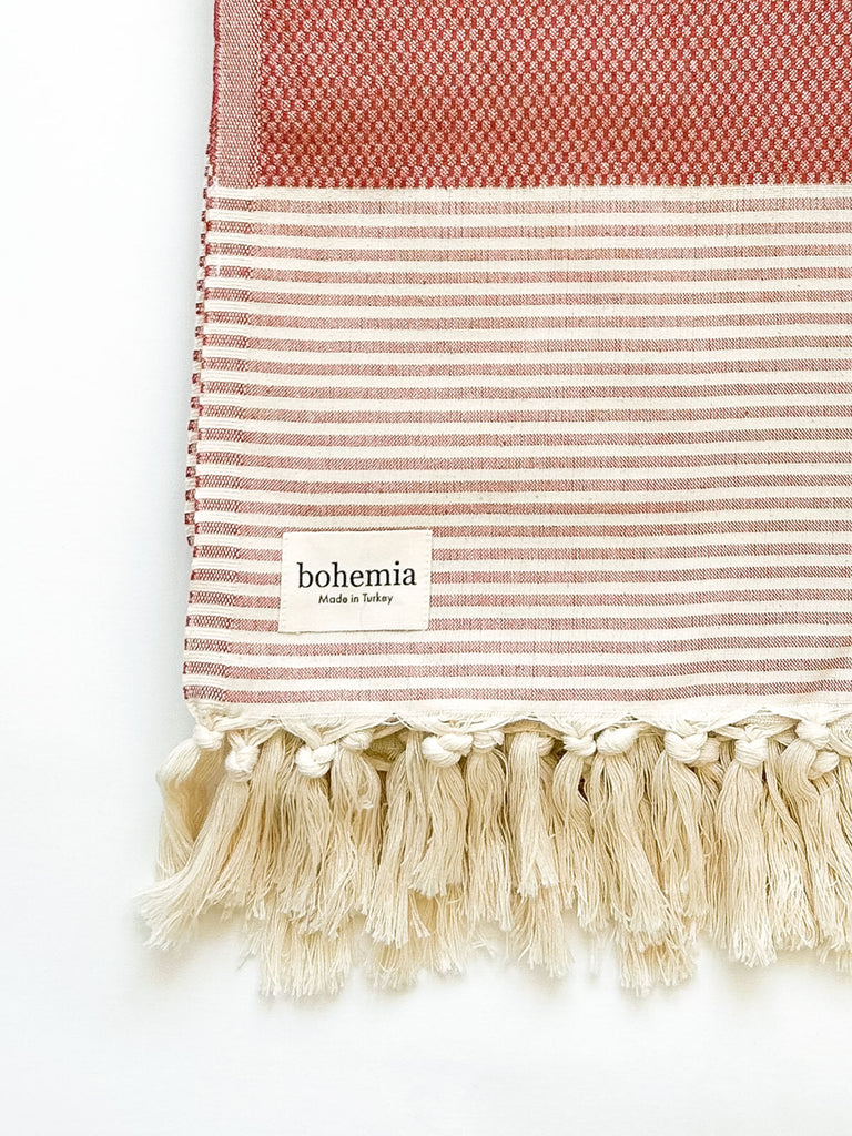 Turkish Cotton Towel in terracotta, showcasing its striped pattern, hand-rolled tassel fringe details, and Bohemia label