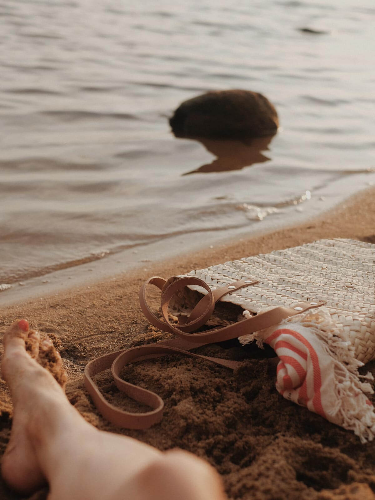 An natural woven Asilah basket with long leather straps on a beach with a hammam towel