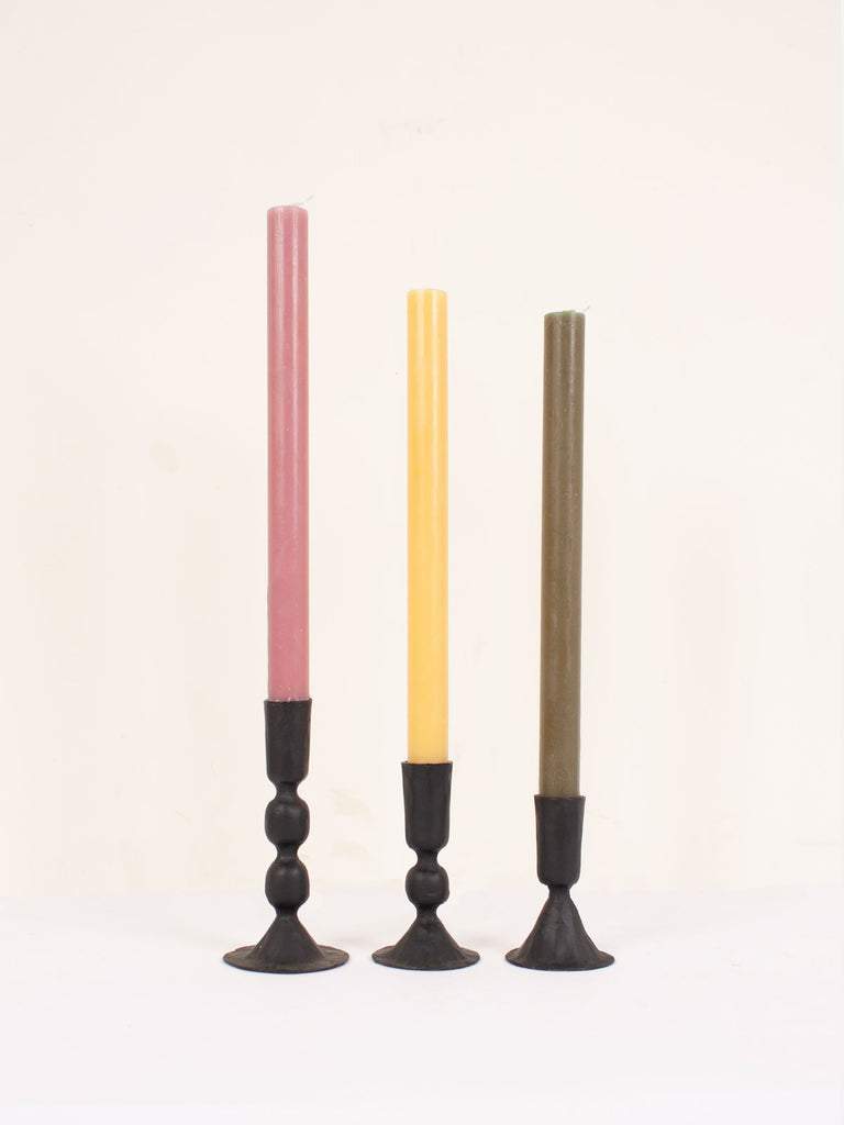 Three handmade black iron candle holders holding colourful candles