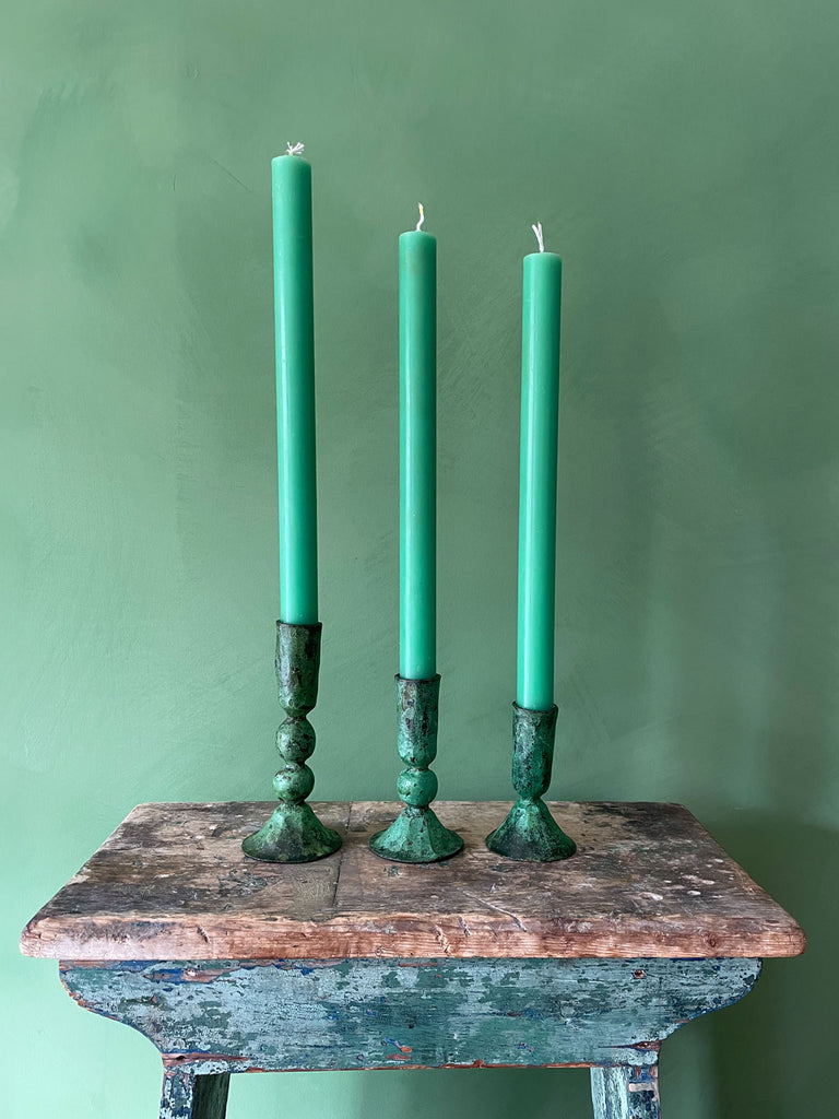 A set of three Austen candle holders in verdigris patina finish, paired with matching candlesticks against a green wall by Bohemia Design