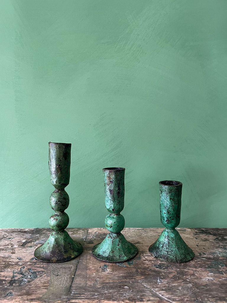 Set of iron candle holders in a verdigris finish, arranged on a wooden stool against a vibrant green wall | Bohemia Design