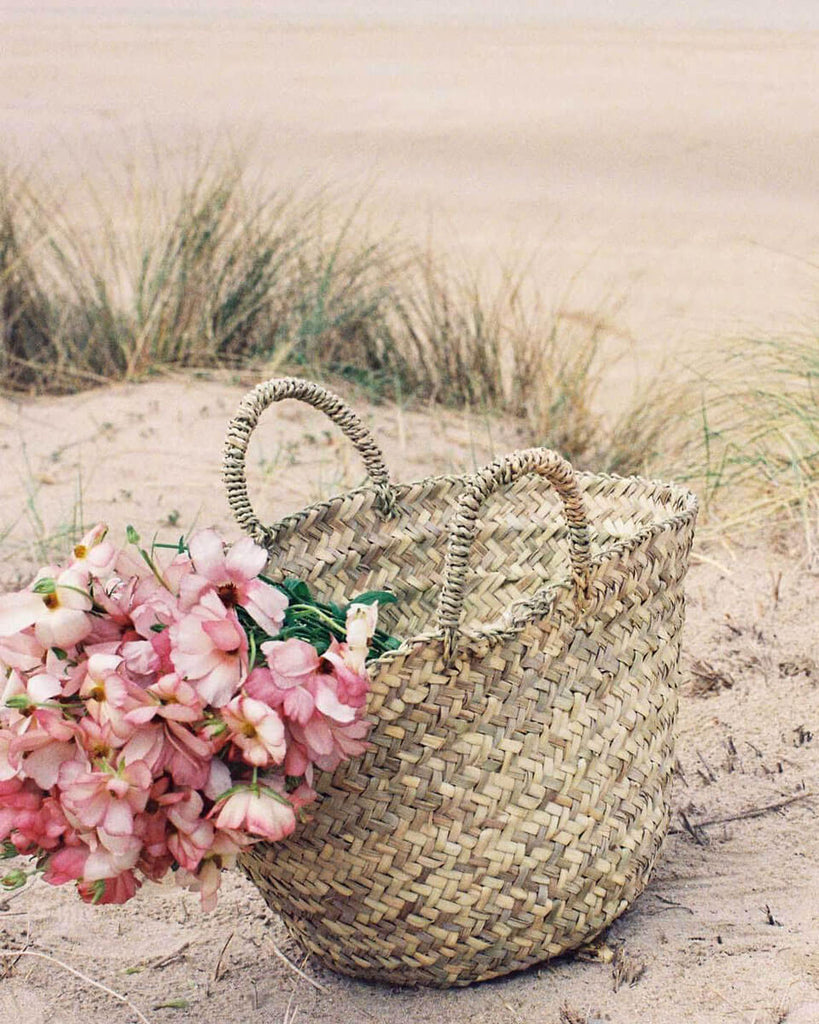 Bohemia Beldi Basket filled with pink flowers on a sandy beach