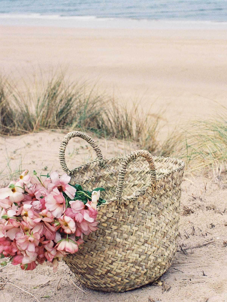 Mini Beldi Basket filled with pink flowers on a beach