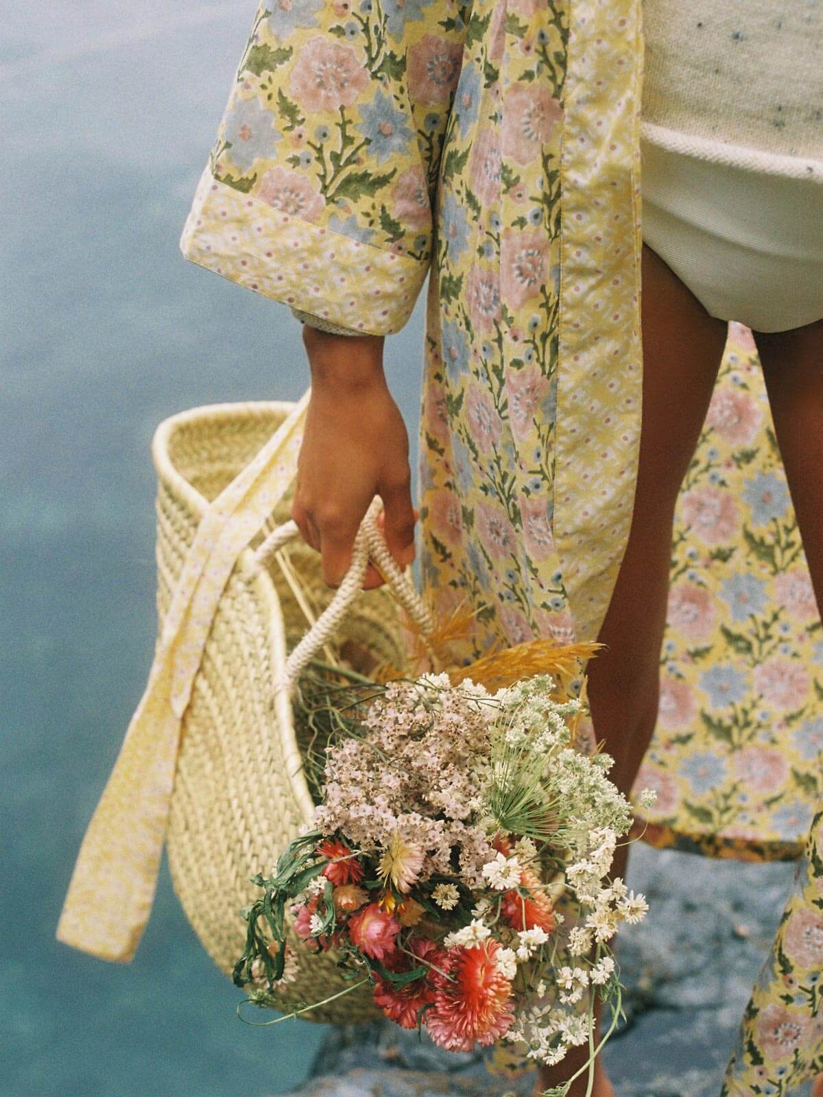 A model wearing a buttermilk yellow block print robe with a basket of dried flowers