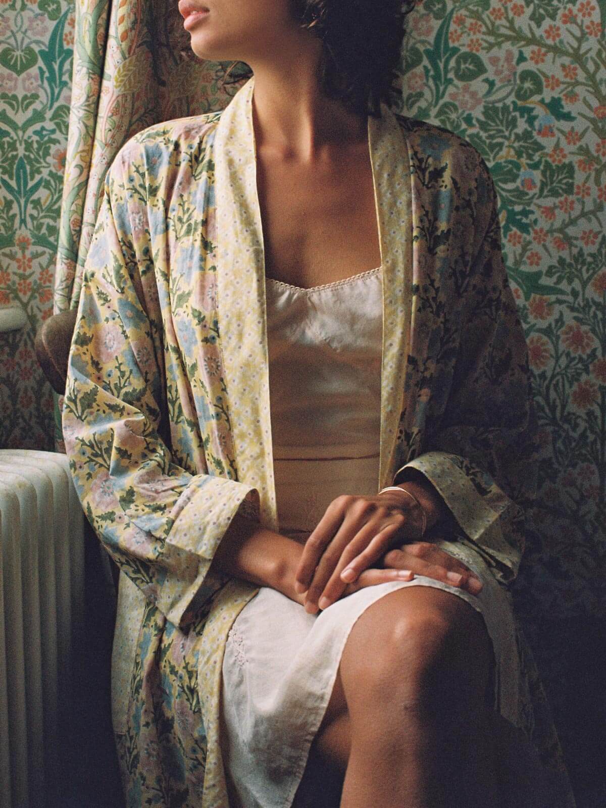 Model sitting by a window wearing a buttermilk yellow block print robe and delicate slip dress.