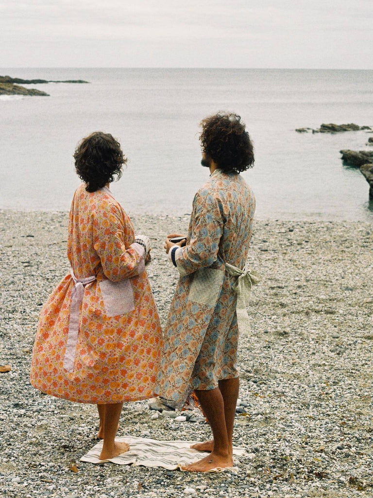 A male and female model on a pebble beach wearing duck egg and lilac block print robes.