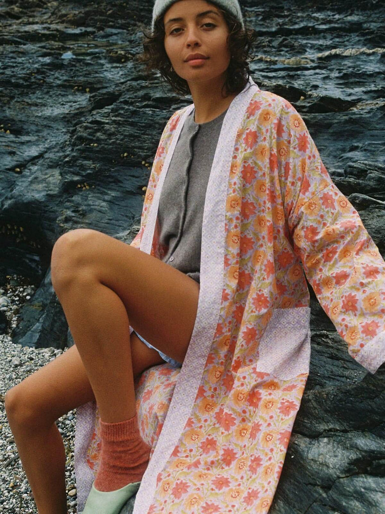 Model on a pebble beach wearing a cosy knit, hat and lilac block print robe and Bohemia babouche slippers.