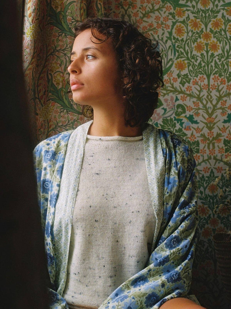 Model sitting by a window wearing a sage floral block print robe in front of floral wallpaper