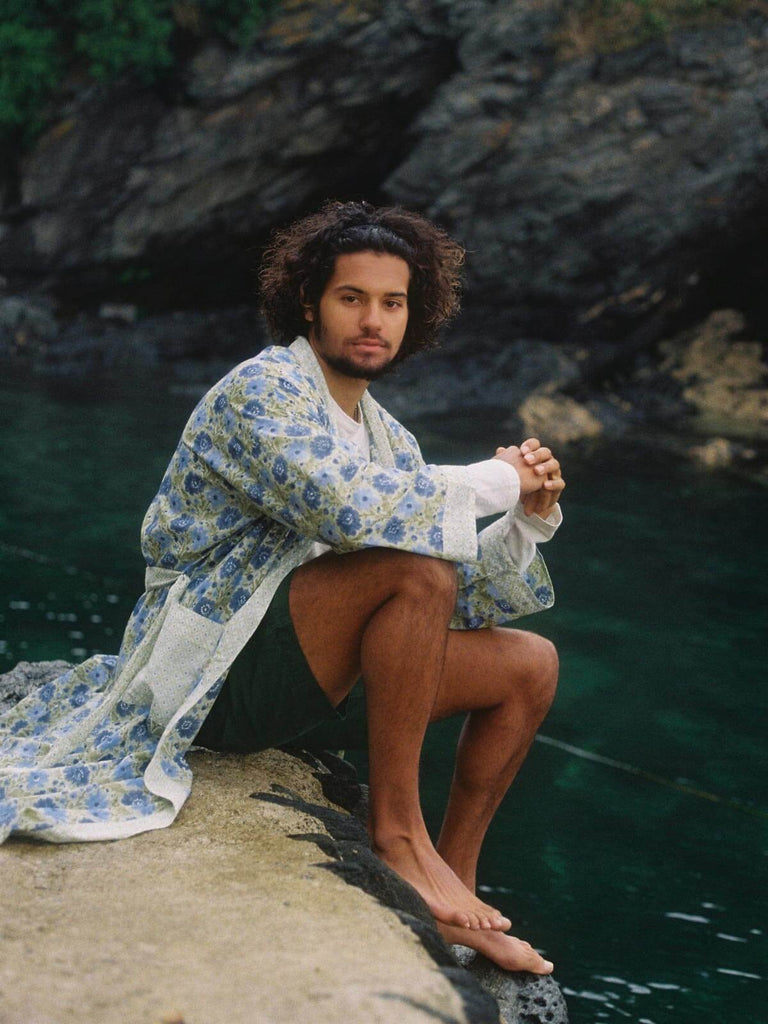 Male model sitting by the sea wearing a sage floral block print cotton robe.