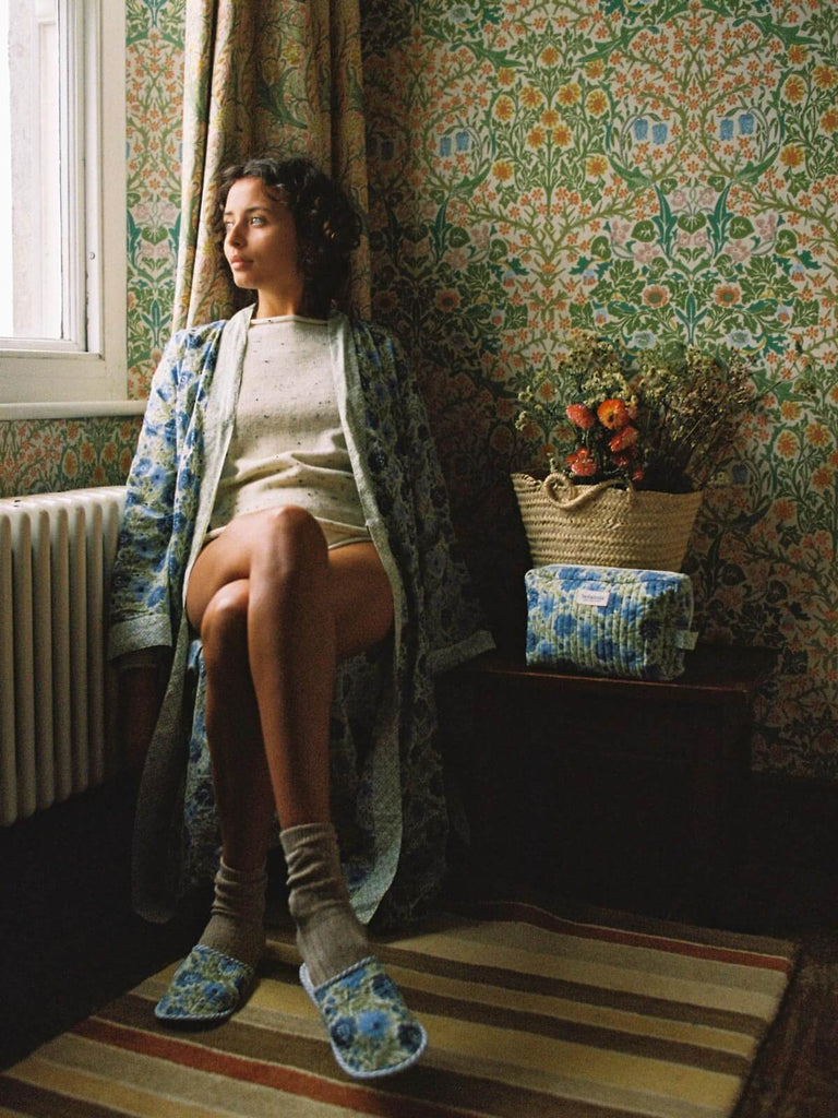 Model by a window in a country house wearing a sage block print robe and matching quilted house slippers.