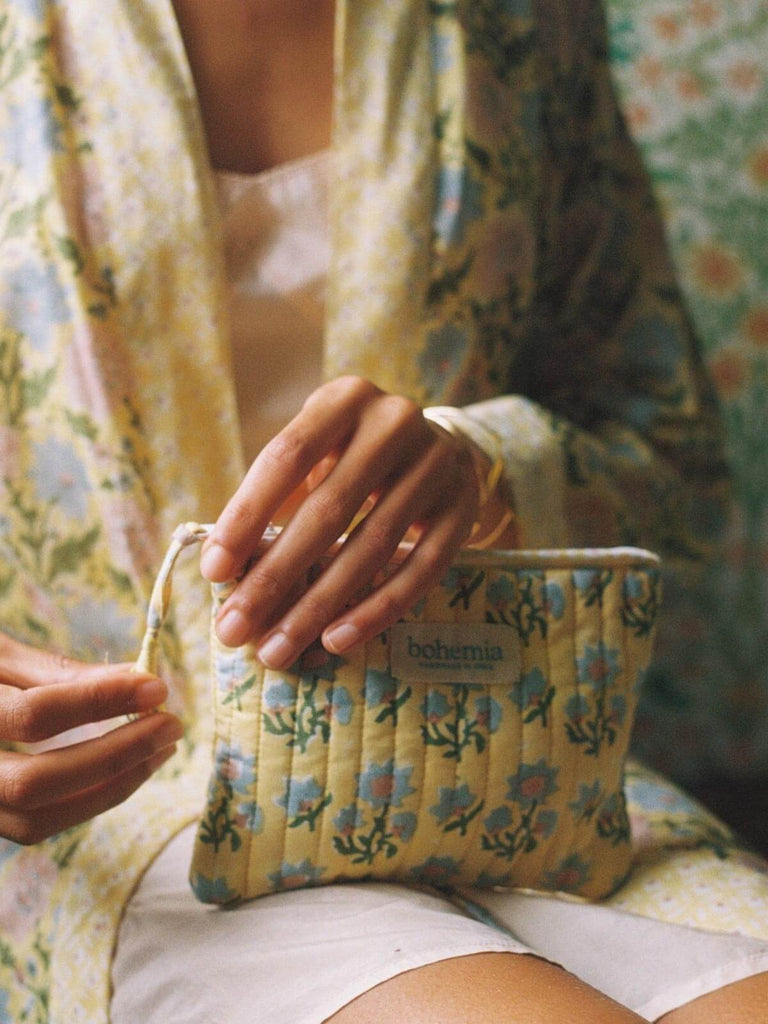 Model holding a buttermilk yellow Posie zip pouch wearing a matching block print robe