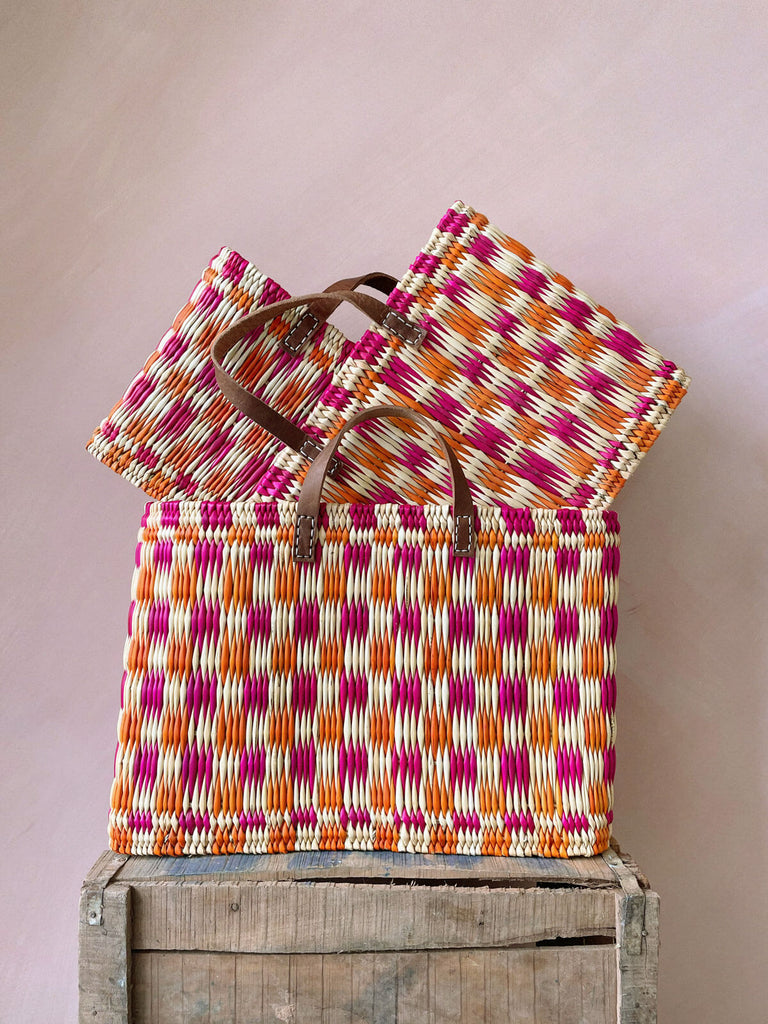 Set of three handwoven chequered reed basket in pink and orange with short leather handles