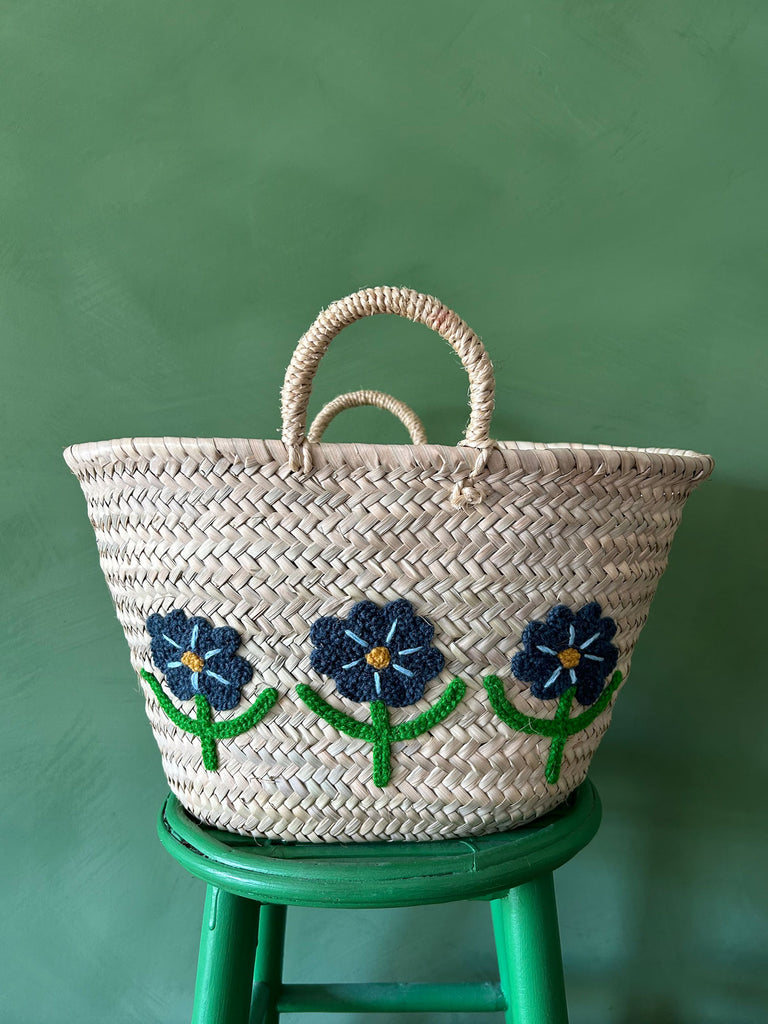 Close-up of a hand-embroidered market basket with daisies against a vibrant green wall by BohemiaDesign
