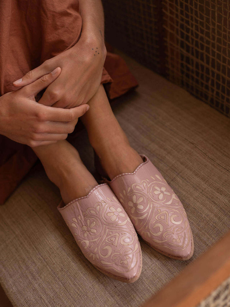 Model sitting wearing a pair of decorative babouche slippers in vintage pink