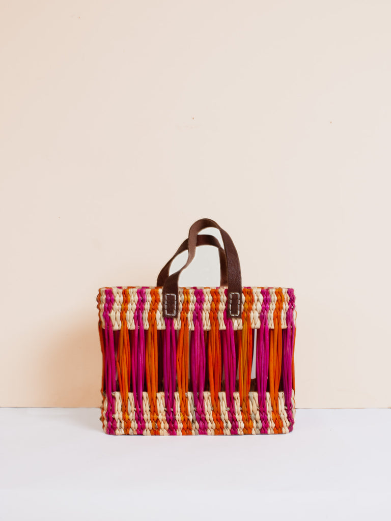 Small decorative reed basket with pink and orange stripes with two short leather handles