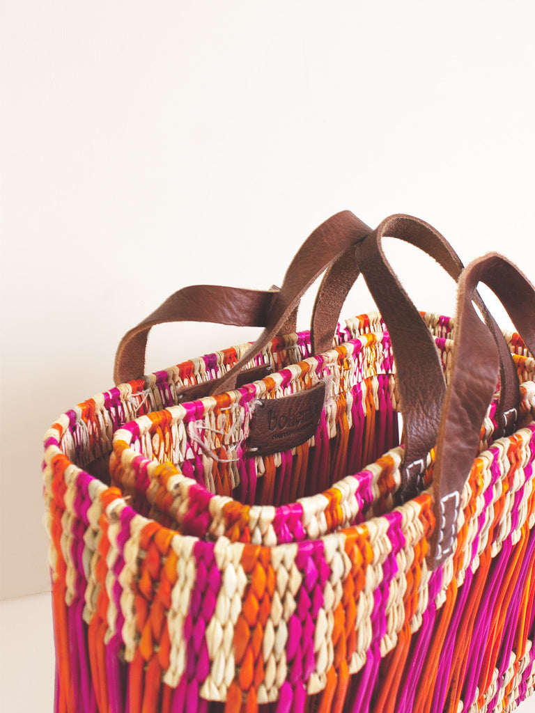 Two decorative reed baskets in pink and orange stacked together with tan leather handles