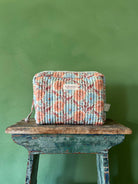 A Floribunda washbag in duck egg, placed on a rustic stool against a green wall