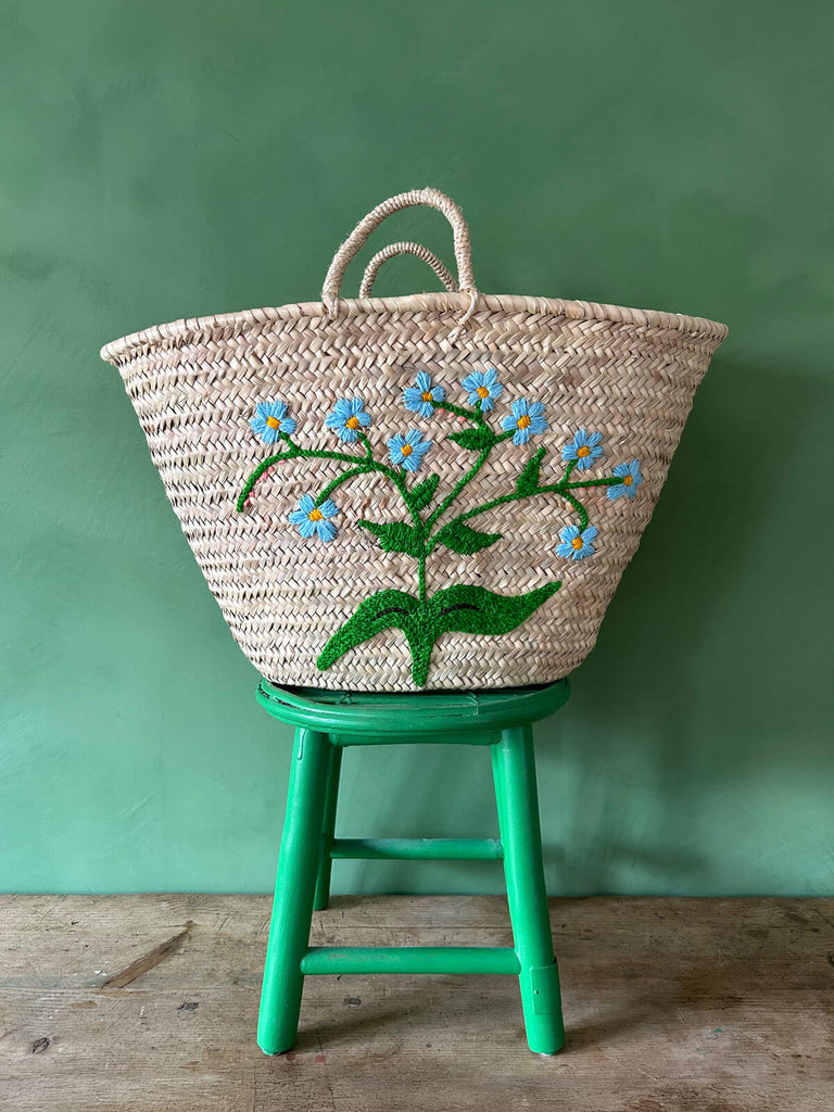 Wholesale woven market basket with a embroidered Forget-Me-Not floral motif, set against a green wall | Bohemia Design