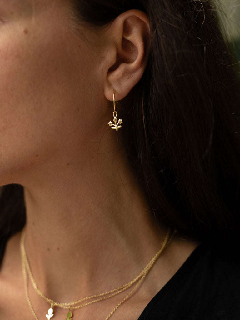 Model wearing wholesale gold hoop earrings with delicate posie flower charm