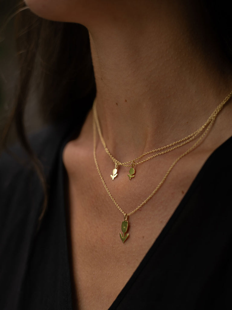 Model wearing layered gold flower necklaces with tulip and daisy pendants on fine gold chains