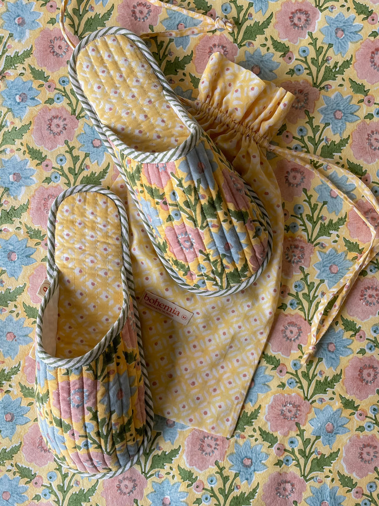 Bohemia carpet slippers with cotton drawstring bag, set against a matching floral-patterned background, Buttermilk.