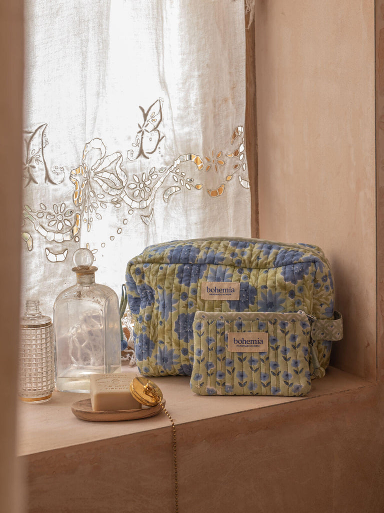 Sage blue and green washbags of different sizes in a bathroom shelf next to handmade soap and antique bottles