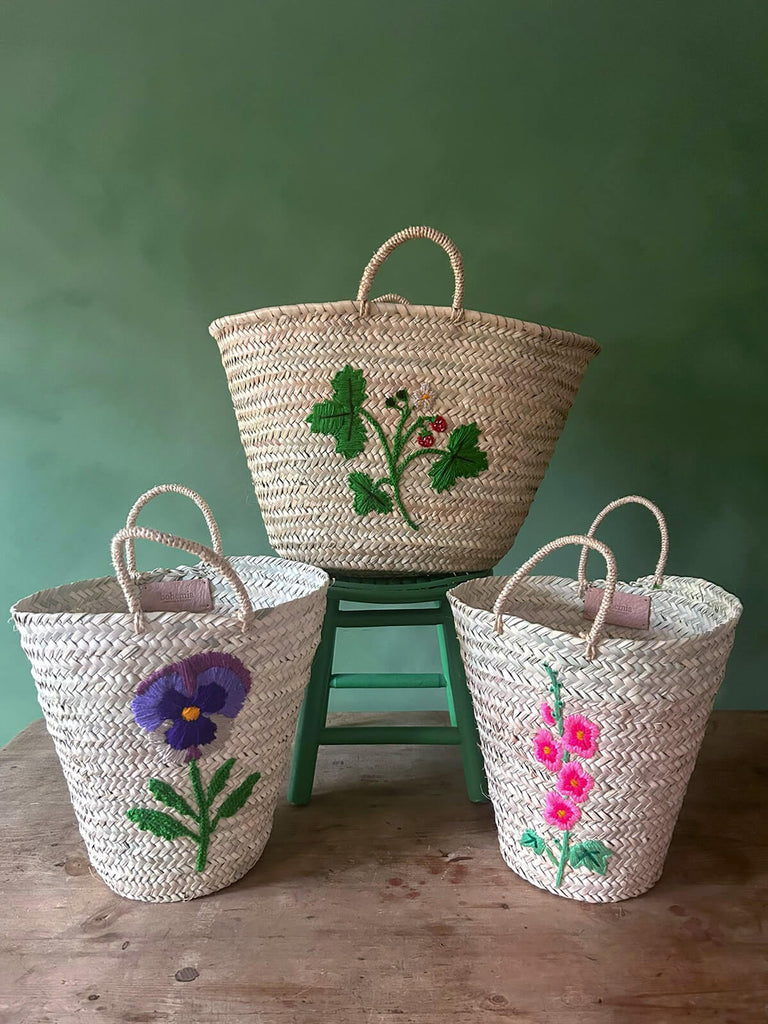 A group of natural hand-woven Moroccan baskets featuring three new exquisite hand-embroidered botanical and floral designs  by Bohemia Design Wholesale