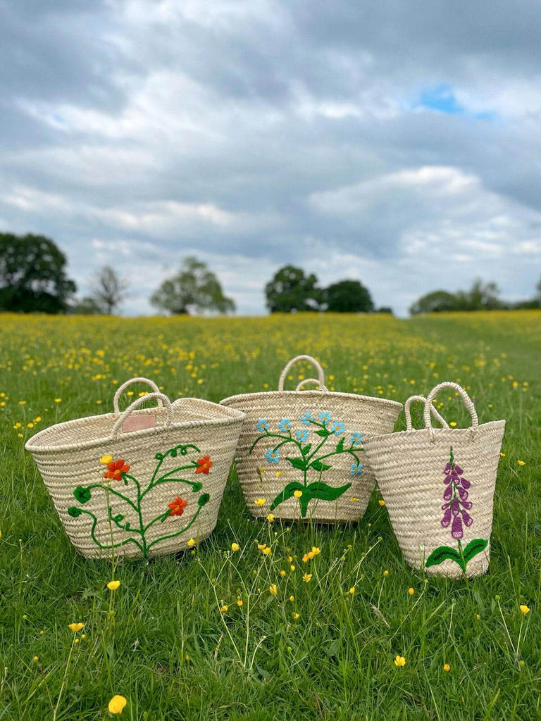 Hand-embroidered wholesale Moroccan baskets in three unique floral designs on a green meadow of tiny yellow flowers by Bohemia Design