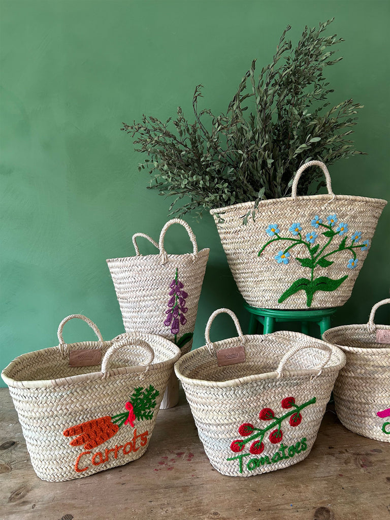A group of wholesale Moroccan, hand-embroidered baskets set against a lush green wall, curated by Bohemia Design