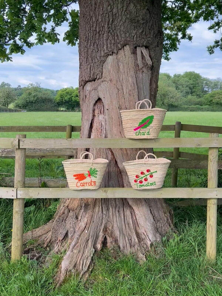 Hand embroidered market basket bags featuring three vegetable designs, all resting on a wooden fence in an outdoor setting | Bohemia Design