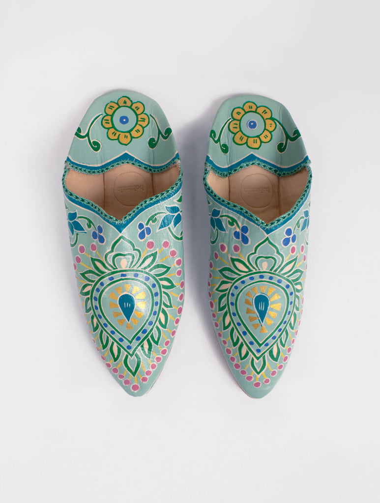 A pair of pointed babouche slippers in a sage green leather with exquisite hand painted, nature inspired elements and golden highlights,